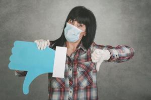 young woman wearing medical mask for coronavirus holding a dislike icon photo