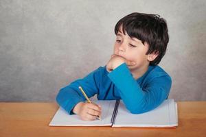 niño triste y pensativo con un libro sobre fondo gris foto