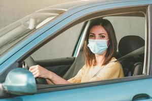 mujer joven conduciendo un coche con una máscara médica en la cara foto