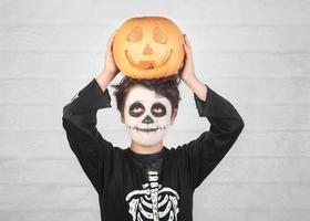 feliz halloween niño divertido en un disfraz de esqueleto con calabaza de halloween sobre su cabeza foto