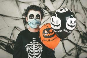 Happy Halloween. kid wearing medical mask in a skeleton costume with halloween balloons photo