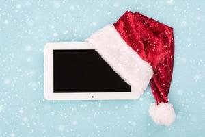 concepto de navidad background.tablet digital en sombrero de santa claus con copos de nieve foto