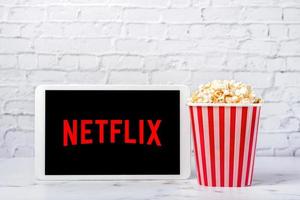 Netflix logo on the screen of a white digital tablet with popcorn