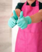 woman in latex gloves and pink apron holding thumbs up as a hope symbol. Ok, hope, win concept photo