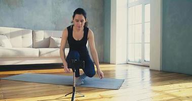 blogueira de fitness mulher liga a câmera no smartphone fixado no tripé para gravar vídeo na sala de estar em câmera lenta de quarentena