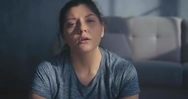 Pretty brunette sweaty lady wearing grey t-shirt rests breathing heavily after intensive training in room closeup slow motion