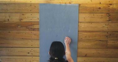 Slim dark haired woman in stylish tracksuit stands in plank position on grey mat in light room view from above slow motion video