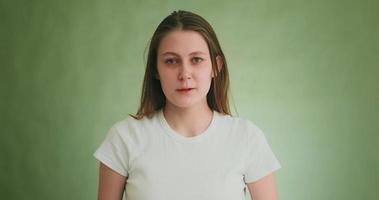 Worried blonde woman in t-shirt wipes tears by hands posing for camera by green studio wall at audition closeup slow motion video