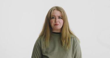 Upset blonde woman in green sweatshirt touches neck posing for camera near studio white wall at audition closeup slow motion video