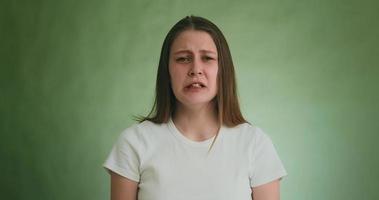 mulher muito ofendida em camiseta branca chora alto com careta triste posando para a câmera perto da parede verde na audição em câmera lenta
