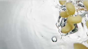 La pasta cavatappi seca cae al agua con pequeñas burbujas para cocinar sobre fondo blanco tiro bajo el agua muy cerca a cámara lenta video