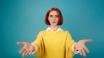 Emotional lady in yellow pullover talks with smile and raises hands back blue background in studio slow motion close view video