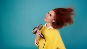 Lady model in yellow sweater sings into hairdryer as microphone in studio at audition on blue background slow motion close view