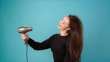 Professional brunette actress with long loose hair plays theatrical sketch singing into hairdryer as mic and shakes head slow motion close view