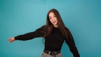 Professional dancer young woman brunette in black pullover performs and smiles on blue studio background slow motion close view video