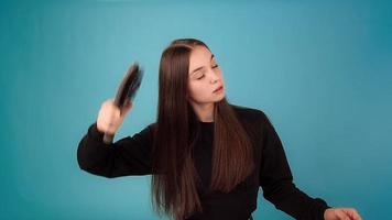 Lady model in black pullover brushes with hairbrush and looks at lost hair with shock in azure studio slow motion close view