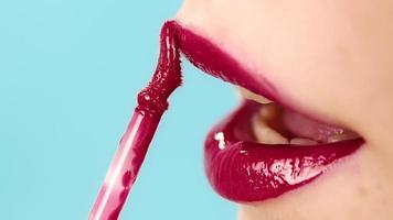 Sorgfältiges Damen-Make-up-Model trägt rot leuchtenden Lippenstift mit speziellem Pinsel auf Blau im Studio-Zeitlupen-Makro auf die Lippen auf video