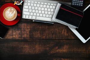 mesa de escritorio de oficina de madera con muchas cosas tableta, computadora portátil, teléfono inteligente, bloc de notas y bloc de notas de taza de café. vista superior con pantalla de iconos de interfaz virtual de espacio de copia. foto