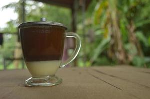 serving coffee with a clear glass and condensed milk underneath.  outdoor wooden background. photo