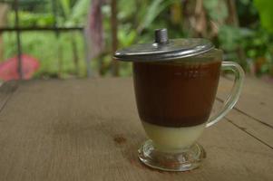 serving coffee with a clear glass and condensed milk underneath.  outdoor wooden background. photo