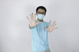 Young asian man wear hygienic mask is scared or panicking with gesturing stop hand. Afraid of coronavirus infection or respiratory illnesses such as flu. Indonesian man isolated on white background photo