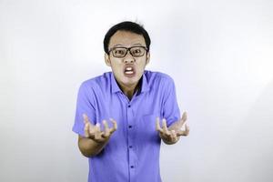 Young Asian Man wear blue shirt is funny angry face with shouting and pointing finger at camera isolated over white background photo