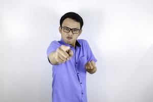 Young Asian Man wear blue shirt is funny angry face with shouting and pointing finger at camera isolated over white background photo