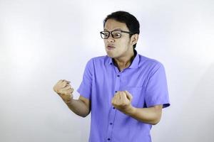 El joven asiático que usa camisa azul es una cara graciosa y enojada con gritos y señalando con el dedo a la cámara aislada sobre el fondo blanco. foto