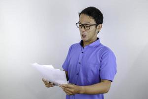 Young Asian Man is mad and angry when looking on paper document. Indonesian man wearing blue shirt. photo