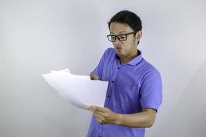 el joven asiático está enojado y enojado cuando mira un documento en papel. hombre indonesio con camisa azul. foto