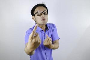 Young Asian Man wear blue shirt is funny angry face with shouting and pointing finger at camera isolated over white background photo