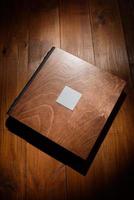 Photo book in a wooden cover on a wooden table. Hard light