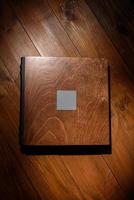 Photo book in a wooden cover on a wooden table. Hard light