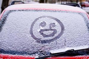 cara sonriente alegre en el parabrisas nevado de un coche foto