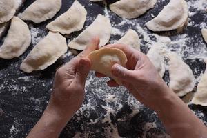 Woman sculpts dumplings with handmade potatoes on a black background. Shot from the top angle. Ukrainian folk cuisine. photo