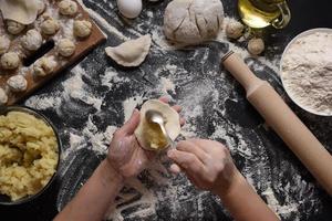 Woman sculpts dumplings with handmade potatoes on a black background. Shot from the top angle. Ukrainian folk cuisine. photo