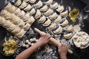 Woman sculpts dumplings with handmade potatoes on a black background. Shot from the top angle. Ukrainian folk cuisine. photo