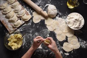 Woman sculpts dumplings with handmade potatoes on a black background. Shot from the top angle. Ukrainian folk cuisine. photo