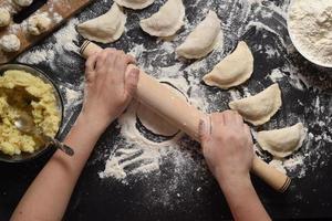 Woman sculpts dumplings with handmade potatoes on a black background. Shot from the top angle. Ukrainian folk cuisine. photo