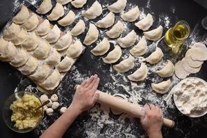 Woman sculpts dumplings with handmade potatoes on a black background. Shot from the top angle. Ukrainian folk cuisine. photo