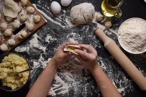 Woman sculpts dumplings with handmade potatoes on a black background. Shot from the top angle. Ukrainian folk cuisine. photo