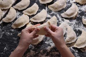 Woman sculpts dumplings with handmade potatoes on a black background. Shot from the top angle. Ukrainian folk cuisine. photo