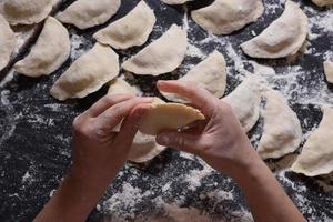 Woman sculpts dumplings with handmade potatoes on a black background. Shot from the top angle. Ukrainian folk cuisine. photo