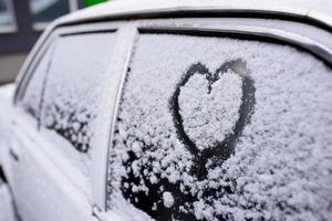 Heart drawn on a car windshield covered with fresh Christmas snow photo