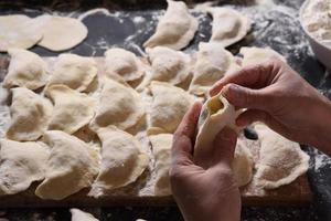 Woman sculpts dumplings with handmade potatoes on a black background. Shot from the top angle. Ukrainian folk cuisine. photo