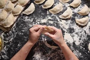 Woman sculpts dumplings with handmade potatoes on a black background. Shot from the top angle. Ukrainian folk cuisine. photo