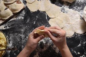 Woman sculpts dumplings with handmade potatoes on a black background. Shot from the top angle. Ukrainian folk cuisine. photo