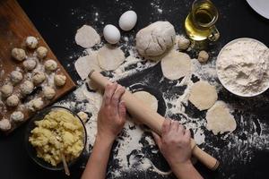 Woman sculpts dumplings with handmade potatoes on a black background. Shot from the top angle. Ukrainian folk cuisine. photo