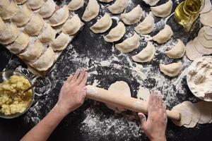 Woman sculpts dumplings with handmade potatoes on a black background. Shot from the top angle. Ukrainian folk cuisine. photo