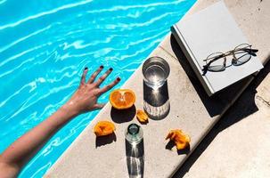 una mano en el agua junto a un libro blanco con vasos y frutas foto